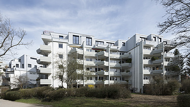 Photo of a multi-storey building with a white façade. Wooden extension.
