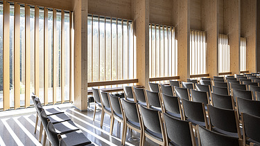 Foto eines bestuhlten Innenraums der Tau Kirke in Norwegen. Man sieht die Holz-Skelett-Struktur der Decke und Holzelemente an der Wand.