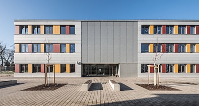 Außenaufnahme der Schule in Erfurt. Man sieht ein großes, weißes Gebäude mit bunten Farbelementen bei den Fenstern.