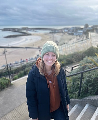 Photo of a young woman. The beach and the sea can be seen in the background.