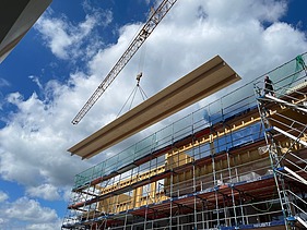 Photo of a timber construction site in Berlin. You can see an overlong ribbed element on the crane.
