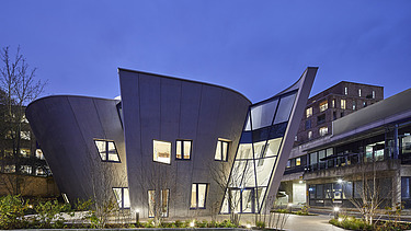 Photo of a building with a wooden façade and sloping walls. Shot at night.