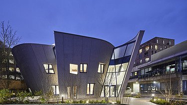 Photo of a building with a wooden façade and sloping walls. Shot at night.