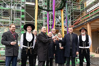 News ZÜBLIN Timber. UmweltHaus Nuremberg project. Everyone is happy about a successful topping-out ceremony. Photo of several people under a topping-out wreath. UmweltHaus Nuremberg project.