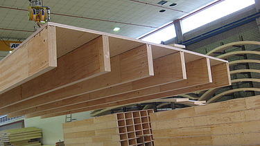 Foto eines Rippenelements am Kran in der Produktionshalle von ZÜBLIN Timber. Im Hintergrund sind auch Kastenelemente zu sehen.