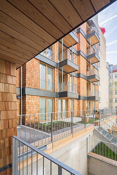 Photo of a multi-storey residential complex made of wood. You can see a detailed section of the façade made of wooden shingles.