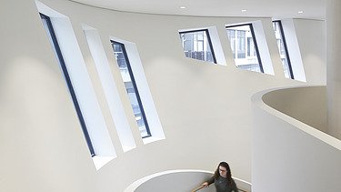 Photo of an interior with white walls. A woman is walking up the stairs.