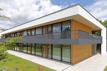 Außenaufnahme der Kita in Frankfurt. Man sieht ein Gebäude aus Holz mit Flachdach.