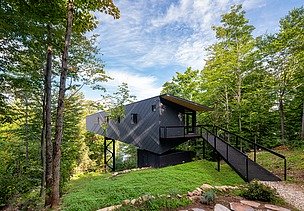 Photo of a wooden house on steel stilts in the middle of the forest.