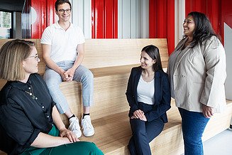 Dual study program at ZÜBLIN Timber Photo of three seated and one standing person in the ZÜBLIN Innovation Center