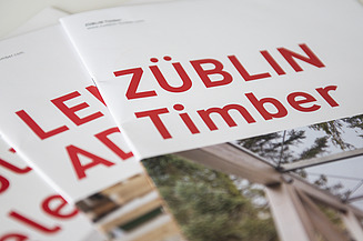 Photo of several brochure covers with red lettering. ZÜBLIN Timber.