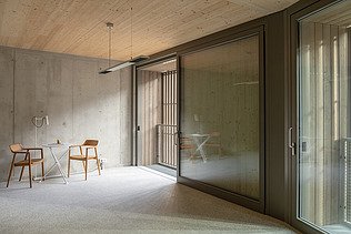 Foto der mehrgeschossigen Wohnanlage in der Stendaler Straße Berlin. Man sieht einen leeren Raum mit Holzdecke und Holzstühlen.