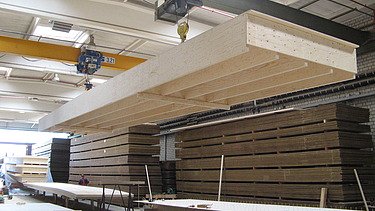 Photo of a large rib element on the crane in the ZÜBLIN Timber production hall.