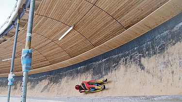 Foto einer Bobbahn mit Holzüberdachung und liegendem Bobfahrer