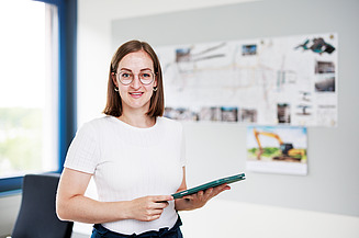 Photo of a young trainee, standing at a computer workstation. Training as a draftswoman.
