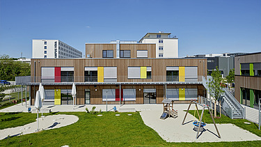 Photo of a kindergarten in Munich. You can see a wooden building with a garden.