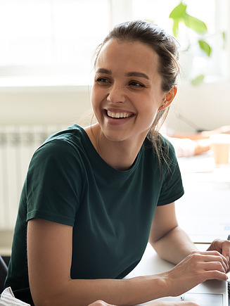 Foto von zwei Frauen die sich anlachen. Sie sitzen vor einem Laptop.