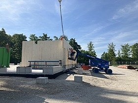 Baustellenfoto, auf dem die Montage der ersten Brettsperrholzelemente zu sehen ist.