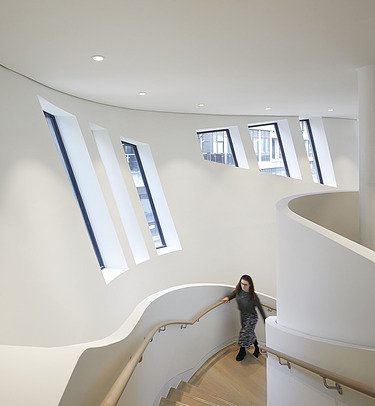 Photo of an interior with white walls. A woman is walking up the stairs.