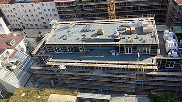 Foto des Rohbaus VINZENT in München. Zu sehen ist ein eingerüstetes, mehrgeschossiges Gebäude von oben.