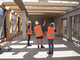 Foto des Rohbaus VINZENT in München. Zu sehen sind drei Männer in Baustellenkleidung.