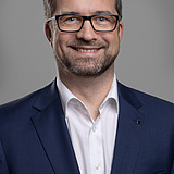 Foto eines lachenden Mannes mit Vollbart und Brille, blauem Jackett und weißem Hemd. Rainer Stettberger.