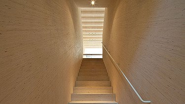 Photo of a wooden staircase with wooden walls in fineline look. Looking upwards.