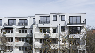 Foto eines mehrgeschossigen Gebäudes mit weißer Fassade. Aufstockung aus Holz.