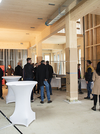 Foto vom Richtfest des Büroneubaus T3 in Aichach. Man sieht einen Innenraum aus Holz mit Menschen.