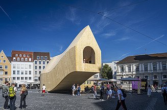 LENO cross laminated timber. Project NEXT500 Pavilion Fuggerei Augsburg Photo of a curved wooden pavilion in LENO cross-laminated timber on Augsburg's town hall square.