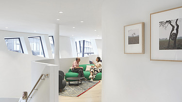 Photo of an interior. Two people are sitting on a green couch. 