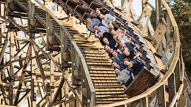 Foto der Holzachterbahn Colossos im Heide Park Resort Soltau. Zu sehen ist ein Teil der Achterbahn und ein Wagon mit Menschen.