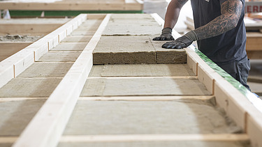 Photo of a LENO ADD element. A commercial employee of ZÜBLIN Timber is placing the wood fiber boards into the element.