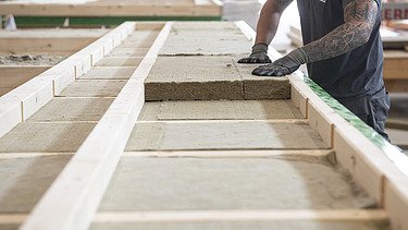 Photo of a LENO ADD element. A commercial employee of ZÜBLIN Timber is placing the wood fiber boards into the element.