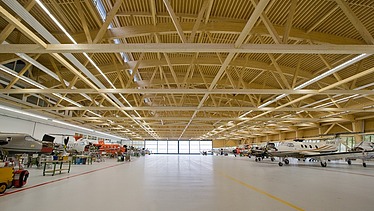 Foto der Montagehalle Pilatus CH-Stans. Zu sehen ist eine große Brettschichtholz-Dachkonstruktion.