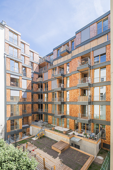 Foto einer mehrgeschossigen Wohnanlage aus Holz. Man sieht einen Detailausschnitt der Fassade aus Holzschindeln.