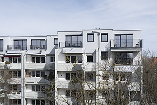 Foto eines mehrgeschossigen Gebäudes mit weißer Fassade. Aufstockung aus Holz.