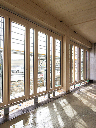 Rohbaufoto eines Innenraums des Büro T3 in Aichach. Man sieht eine Holz-Pfosten-Riegel-Fassade.