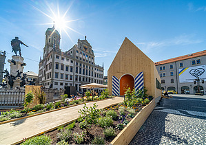 Photo of the NEXT500 pavilion on Augsburg's market square. You can see a modern wooden building.