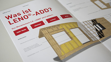 Foto der Innenseite der LENO-ADD-Broschüre von ZÜBLIN Timber. Man sieht einen Wandquerschnitt, der beschrieben wird und eine rote Überschrift.