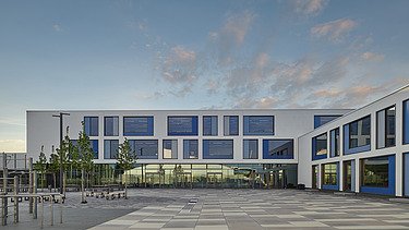 Außenaufnahme des Gymnasiums München-Nord. Man sieht ein großes, weißes Gebäude mit Flachdach.