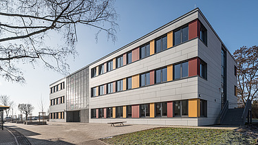 Foto einer Außenaufnahme der Schule Erfurt. Diese hat eine weiße, orange und rote Fassadengestaltung.