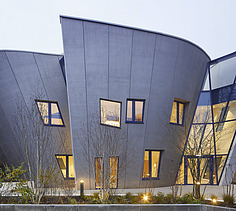 Photo of a building with a wooden façade and sloping walls. Picture at dusk.
