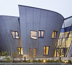 Photo of a building with a wooden façade and sloping walls. Picture at dusk.