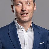 Foto eines lachenden Mannes mit dunklen Haaren, blauem Jackett und weißem Hemd. Daniel Kreißig.