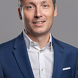 Photo of a smiling man with dark hair, blue jacket and white shirt Daniel Kreißig.