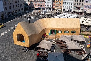 Photo of the NEXT500 pavilion on Augsburg's market square. You can see a modern wooden building.
