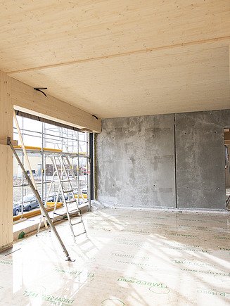Shell construction photo of the interior of the T3 office in Aichach. You can see a wooden ceiling and wooden supports.