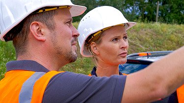 Photo of two people in construction site clothing talking to each other.
