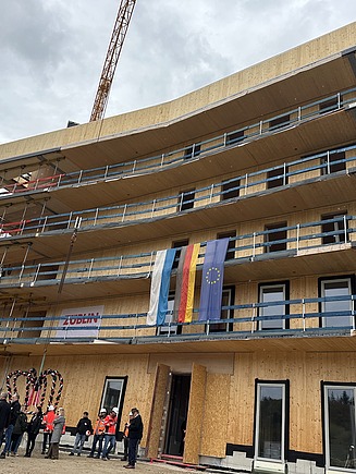 Foto beim Richtfest Grünes Zentrum Landshut. Zu sehen ist ein Holzbau im Rohbau mit Menschen davor.